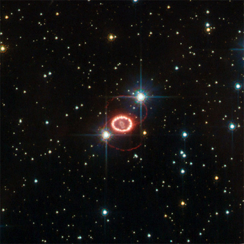 Image of Supernova 1987a, outshines an entire galaxy; the brightest seen from Earth since the invention of the telescope.  Dominating this picture are two glowing loops of stellar material and a very bright ring surrounding the dying star at the centre of the frame.  Although Hubble has provided important clues on the nature of these structures, their origin is still largely unknown. 